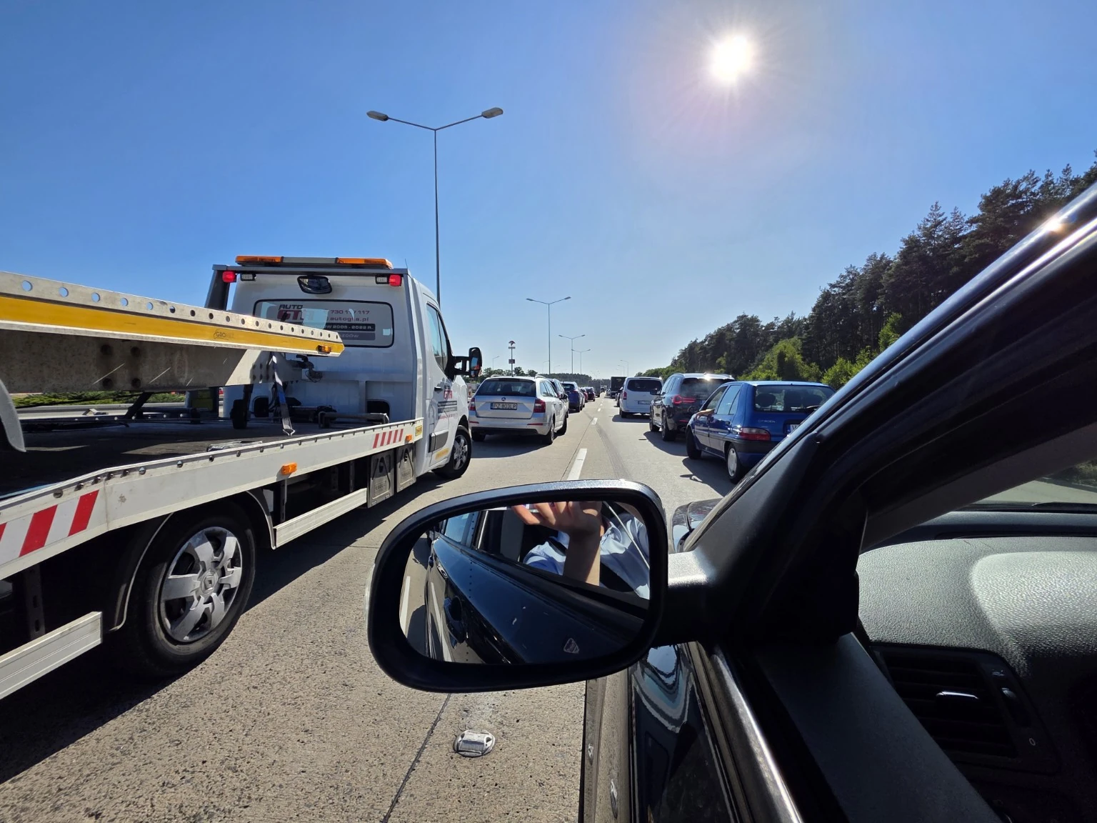 Widok na kolejkę samochodów i lawetę z bocznego okna